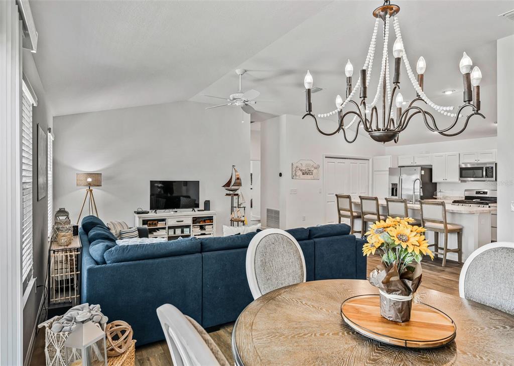 An open-concept living room and kitchen featuring a blue sectional sofa and wooden dining table — 3250 SHERFINSKI AVENUE, THE VILLAGES, FL