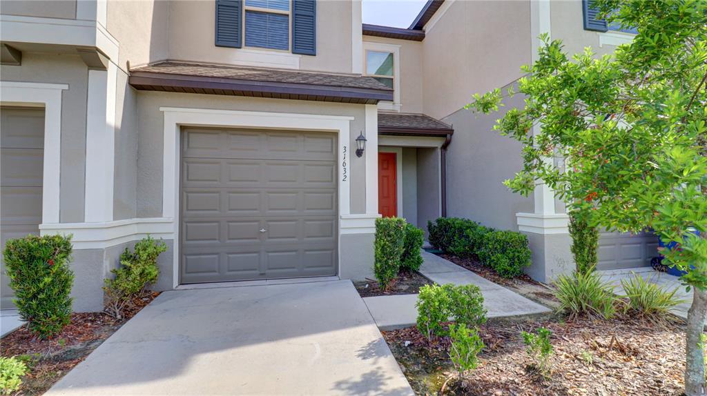 The exterior of a two-story townhouse features a tan facade, a garage, and a red door — 31632 BLUE PASSING LOOP, WESLEY CHAPEL, FL
