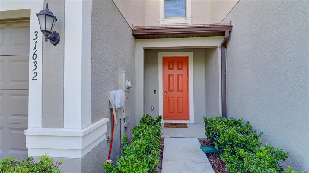 The exterior of a home features a red front door, a walkway, and green bushes — 31632 BLUE PASSING LOOP, WESLEY CHAPEL, FL