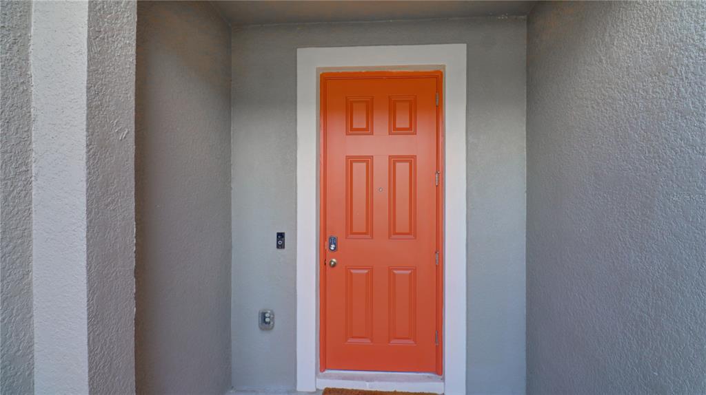 An orange front door with a white frame is set against a gray exterior wall — 31632 BLUE PASSING LOOP, WESLEY CHAPEL, FL