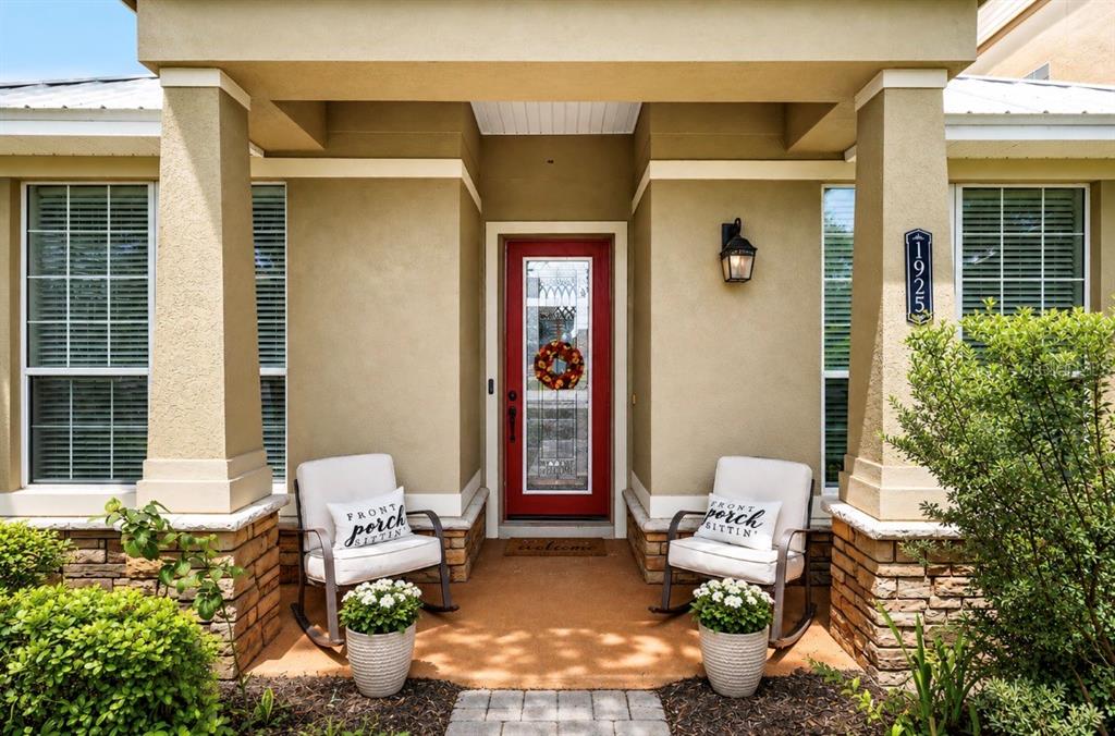 A front porch features two rocking chairs with decorative pillows and a red entry door — 1925 APPALACHEE, TAVARES, FL