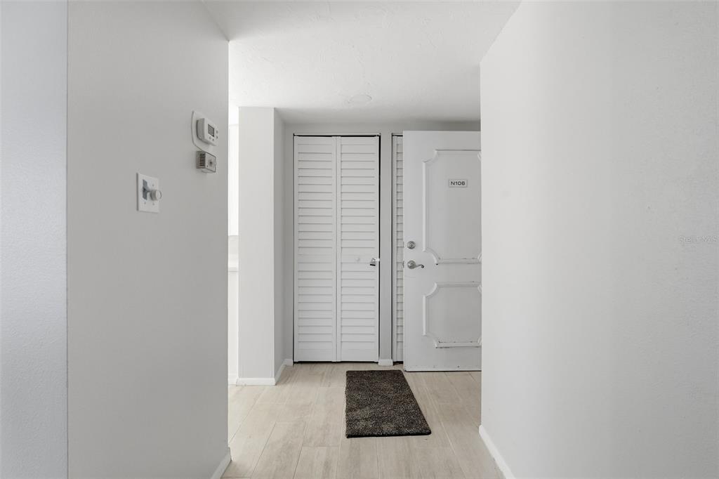 A white-walled entryway features light wood-look flooring, a closet with louvered doors, and a front door — 4440 EXETER DRIVE UNIT 106, LONGBOAT KEY, FL