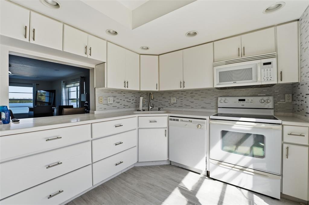 A kitchen features white cabinets, white appliances, a tiled backsplash, and a view of water — 4440 EXETER DRIVE UNIT 106, LONGBOAT KEY, FL