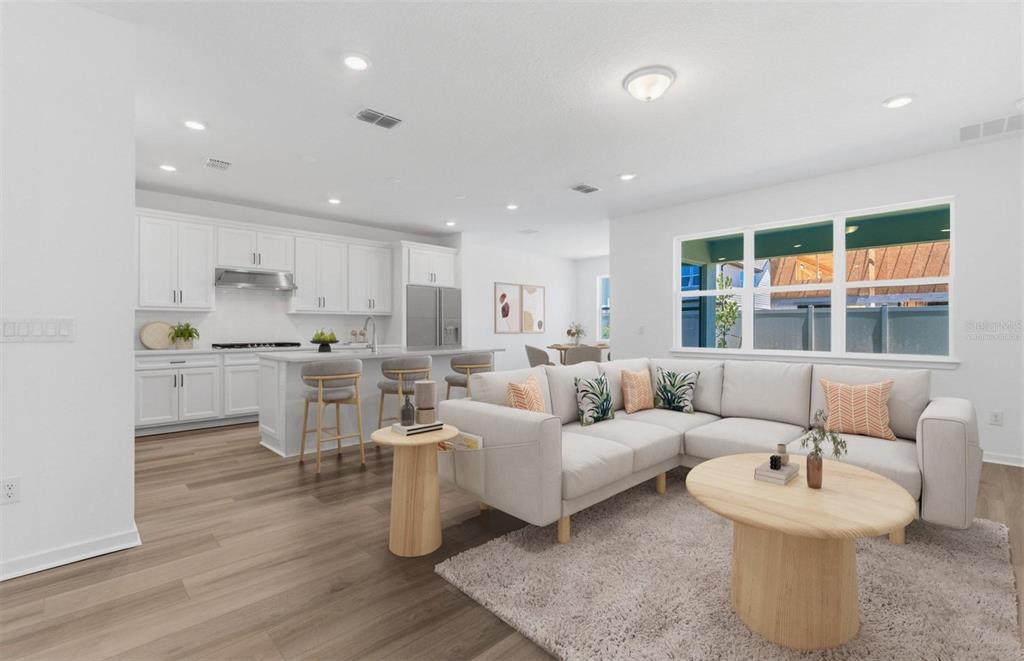 An open-concept living room and kitchen feature white cabinetry, light wood flooring, and neutral furniture — 6979 DEPUE DRIVE, WESLEY CHAPEL, FL