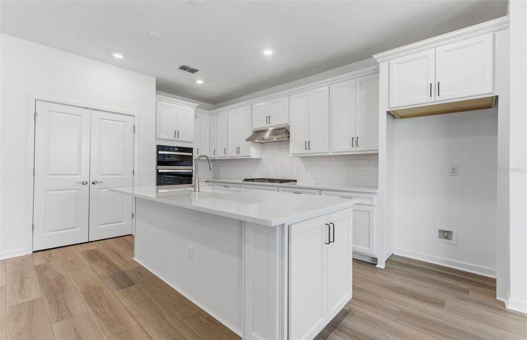 A modern white kitchen features a central island, stainless steel appliances, and light wood flooring — 6979 DEPUE DRIVE, WESLEY CHAPEL, FL