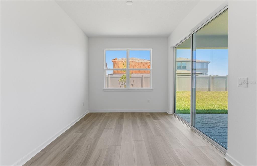 An empty room with light wood-look flooring, white walls, a window, and sliding glass doors — 6979 DEPUE DRIVE, WESLEY CHAPEL, FL