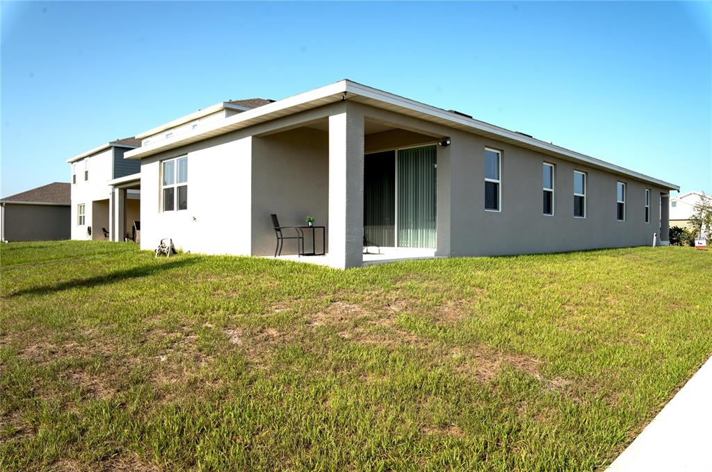 The exterior of a beige house features a covered patio and a large grassy yard — 5503 BLUEBONNET PLACE, HAINES CITY, FL