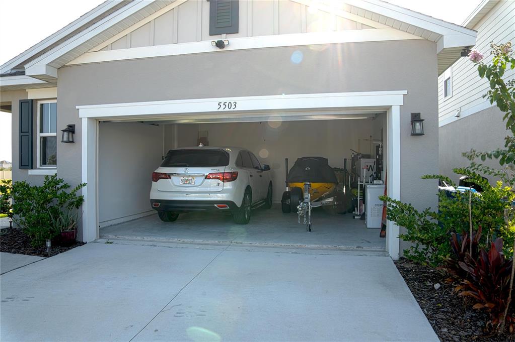 A white SUV and a jet ski on a trailer are parked inside a garage — 5503 BLUEBONNET PLACE, HAINES CITY, FL