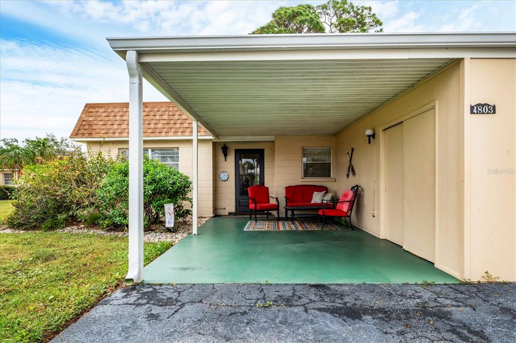 A covered carport features a green painted floor, outdoor seating, and a beige exterior wall — 4803 PARK ACRES DRIVE, BRADENTON, FL