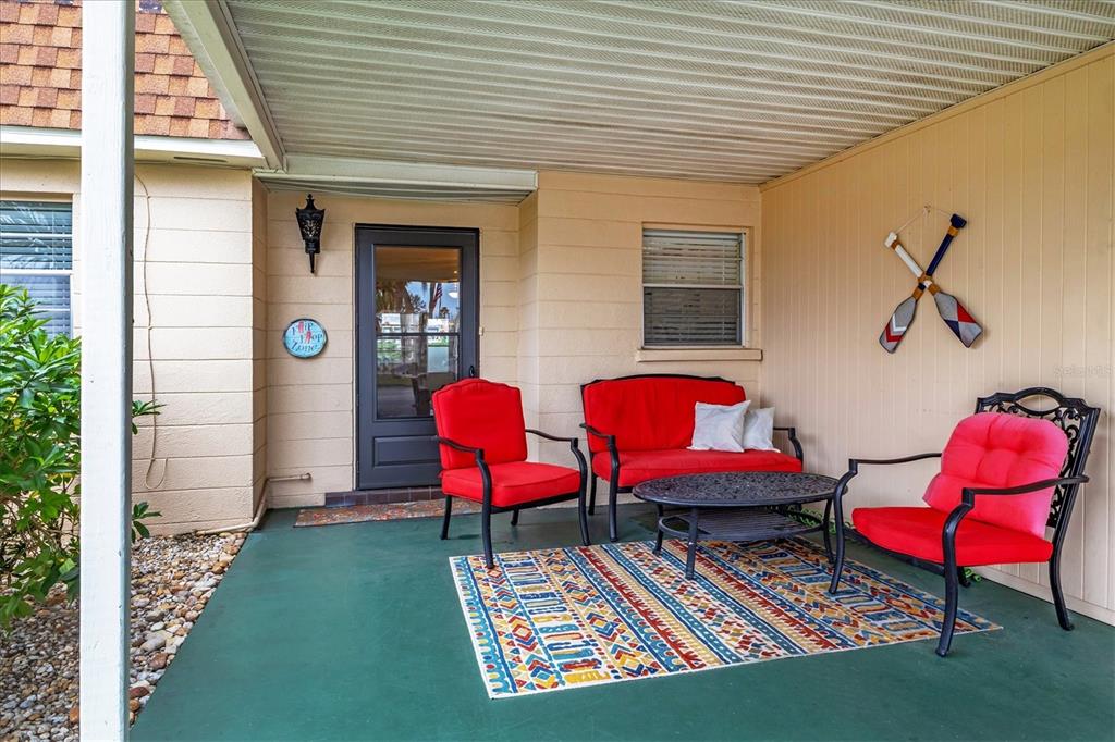 A covered patio features red cushioned outdoor furniture, a patterned rug, and decorative wall oars — 4803 PARK ACRES DRIVE, BRADENTON, FL
