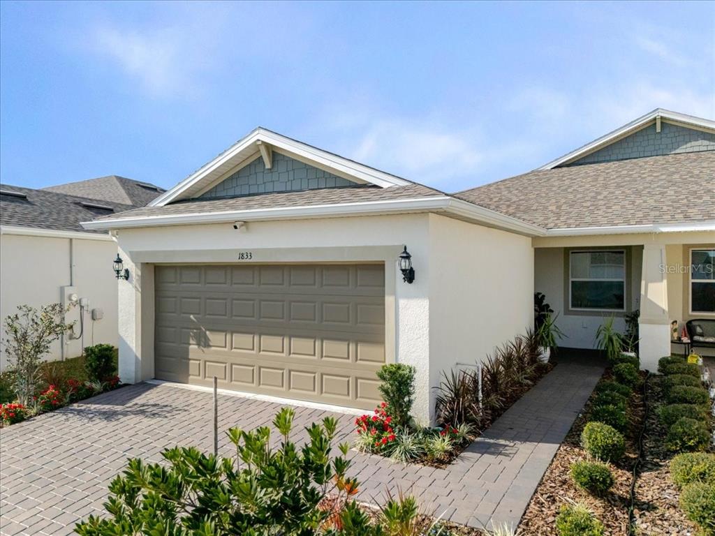 A single-story house exterior features a tan garage, a paved driveway, and a walkway — 1833 SPRING SHOWER CIRCLE, KISSIMMEE, FL