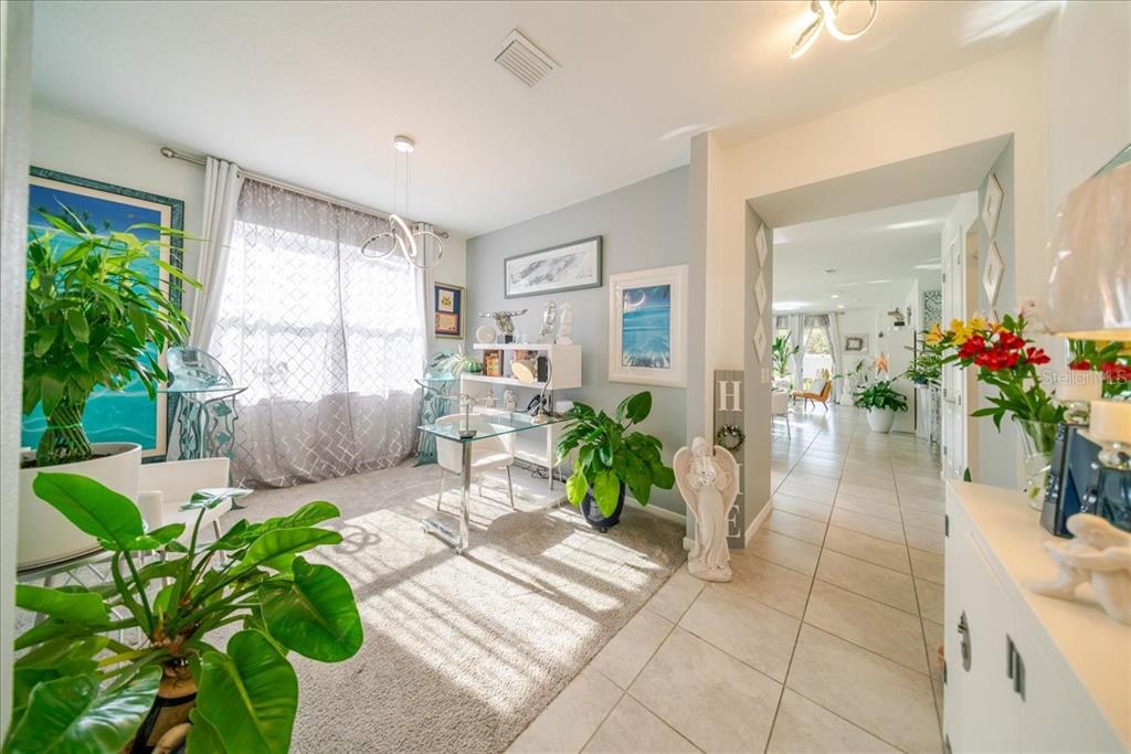 A sunlit home office features a glass desk, carpeted flooring, and several potted plants — 1833 SPRING SHOWER CIRCLE, KISSIMMEE, FL