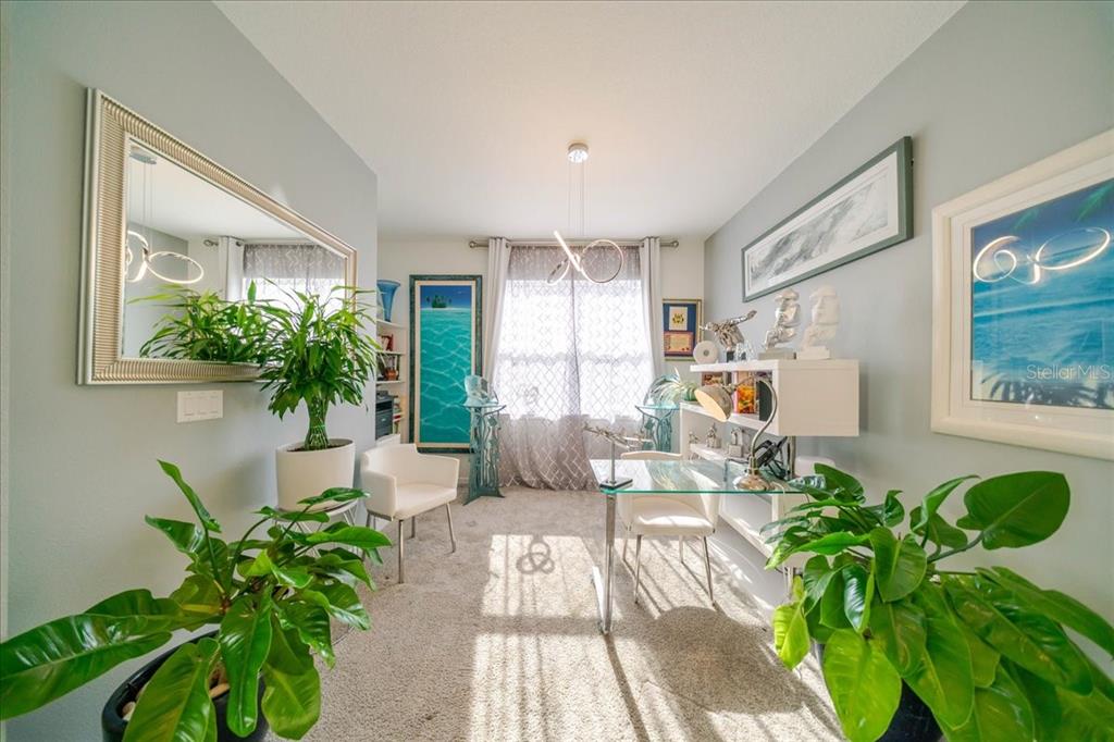 A home office features a glass desk, two white chairs, large plants, and wall art — 1833 SPRING SHOWER CIRCLE, KISSIMMEE, FL