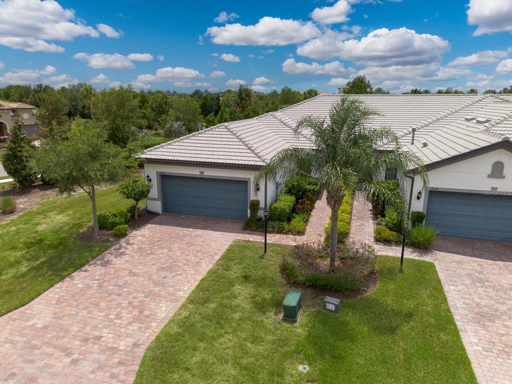 An aerial view of a suburban home with a paver driveway, garage, and palm tree — 17658 CAMDEN DRIVE, BRADENTON, FL