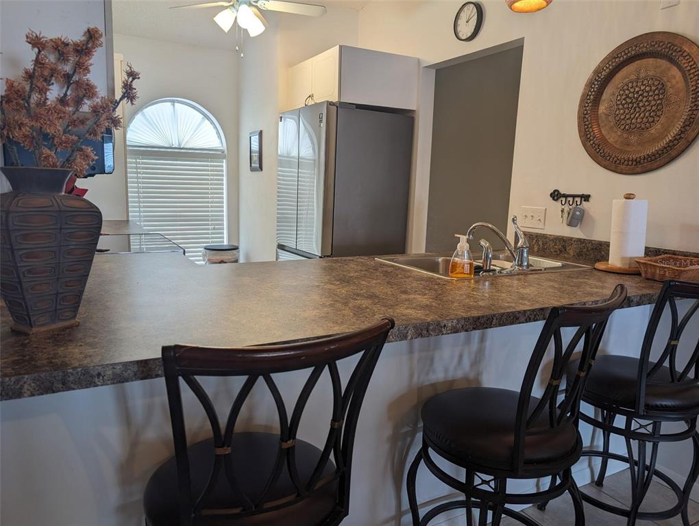 A kitchen features a breakfast bar with two chairs, a stainless refrigerator, and a sink — 308 STEPHEN DRIVE UNIT 8, LAKE PLACID, FL