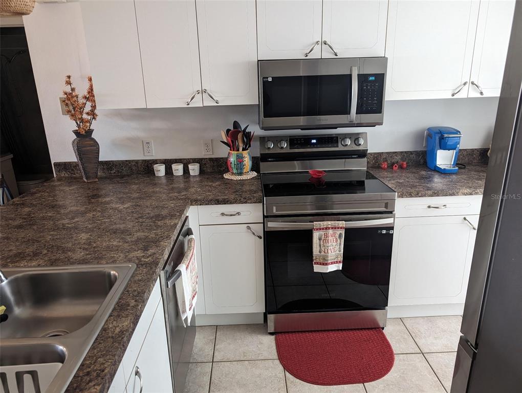 A kitchen features white cabinets, dark countertops, stainless steel appliances, and a red floor mat — 308 STEPHEN DRIVE UNIT 8, LAKE PLACID, FL