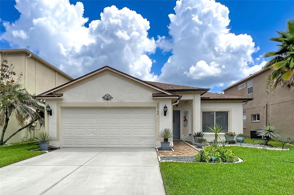 A single-story house with a beige stucco exterior, a two-car garage, and a landscaped yard — 27544 BREAKERS DRIVE, WESLEY CHAPEL, FL