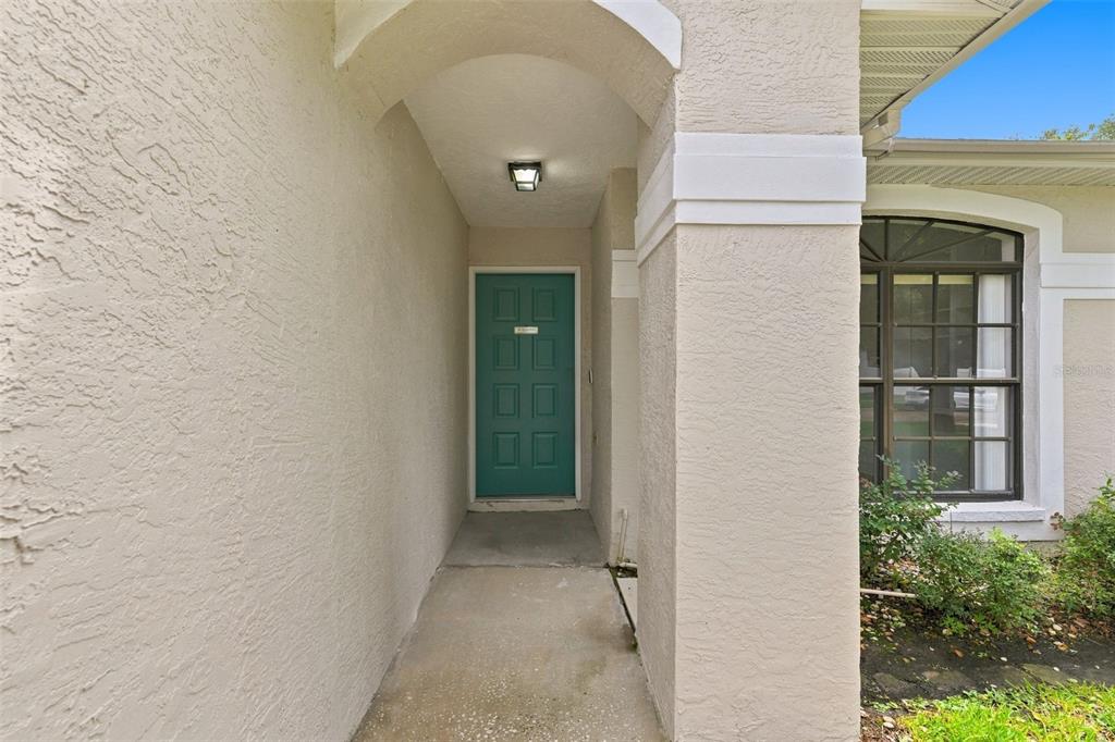 A covered entryway features a teal front door, stucco walls, and a nearby arched window — 1307 FLAXWOOD AVENUE, BRANDON, FL
