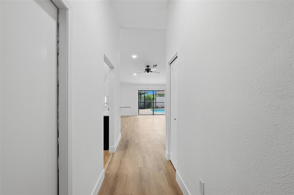 A hallway with light wood flooring leads to an open living area with a pool view — 1307 FLAXWOOD AVENUE, BRANDON, FL