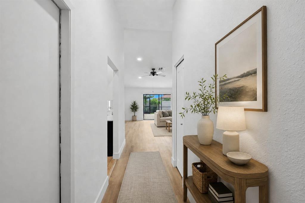 A bright hallway with light wood floors leads to a living room with a ceiling fan — 1307 FLAXWOOD AVENUE, BRANDON, FL