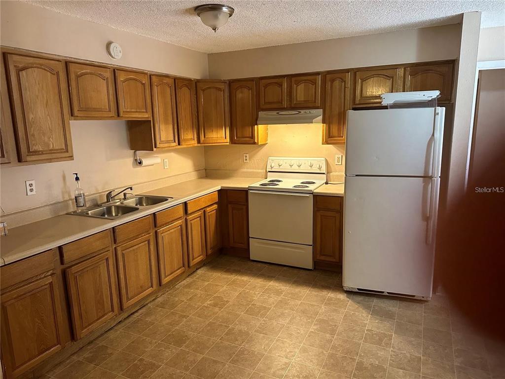A kitchen features wood cabinets, laminate countertops, a white stove, and a white refrigerator — 8203 N KLONDYKE STREET UNIT B, TAMPA, FL
