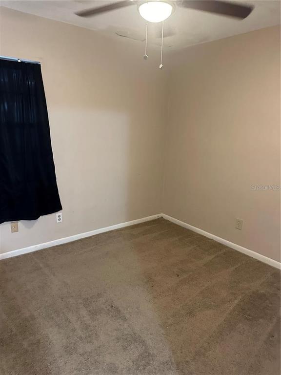 An empty bedroom features beige walls, tan carpeting, a ceiling fan, and a dark curtain — 8203 N KLONDYKE STREET UNIT B, TAMPA, FL