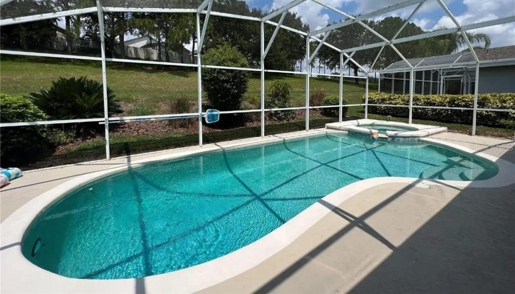 An outdoor swimming pool and attached spa are enclosed within a white screened-in lanai — 143 E WINDSOR PLACE, DAVENPORT, FL