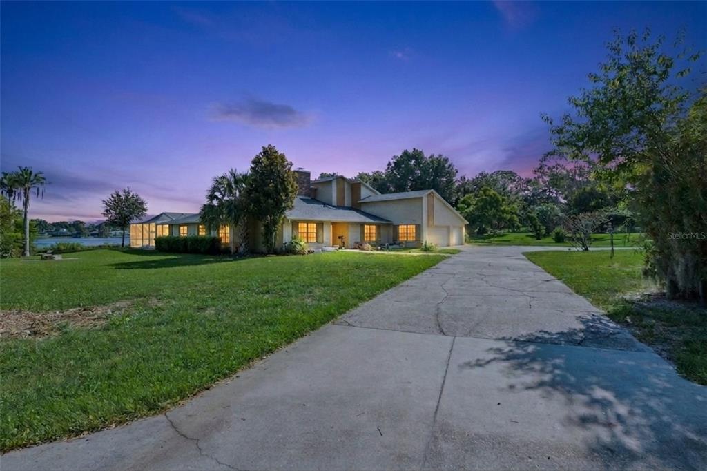 A single-story house with a concrete driveway and a screened porch sits near a lake — 25 LAKEWOOD CAUSEWAY, WINTER HAVEN, FL
