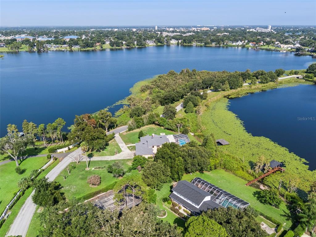 A long concrete driveway leads to a tan house with a two-car garage and trees — 25 LAKEWOOD CAUSEWAY, WINTER HAVEN, FL