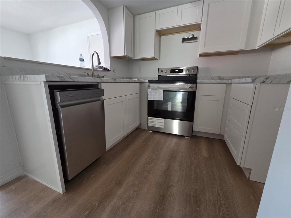 A kitchen features white cabinets, stainless steel appliances, and wood-look flooring — 4812 JASPER DRIVE UNIT 101, NEW PORT RICHEY, FL