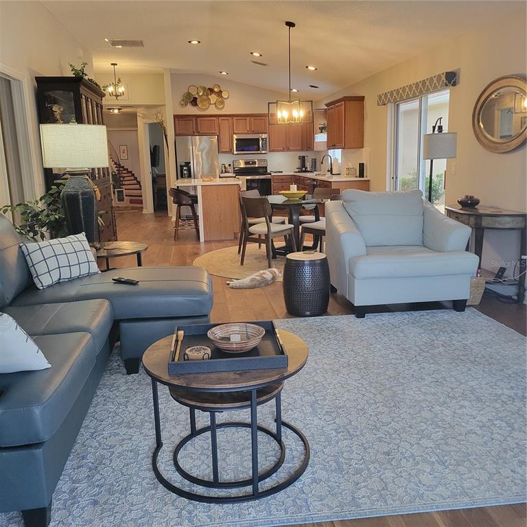 An open-concept living room and kitchen featuring wood flooring, neutral furniture, and a dining area — 1521 TRENTON LANE, THE VILLAGES, FL