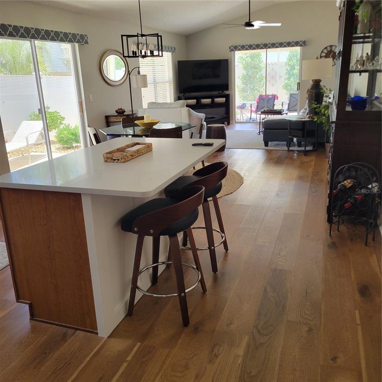 An open-concept kitchen and living area features a white island, wood flooring, and sliding doors — 1521 TRENTON LANE, THE VILLAGES, FL