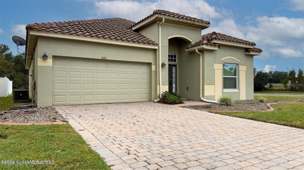 A single-story house with a tan stucco exterior, tile roof, and a paved driveway — 4367 FITZROY REEF DRIVE, MIMS, FL