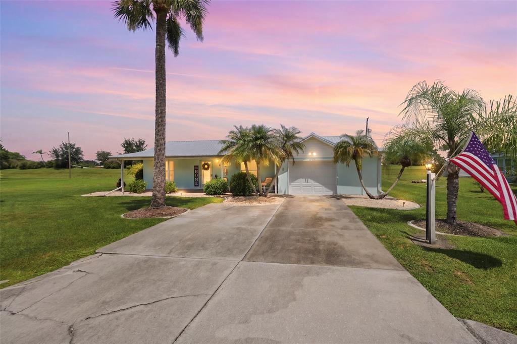 A single-story house with a concrete driveway, palm trees, and an American flag in front — 8451 SW SUNNYBREEZE ROAD, ARCADIA, FL
