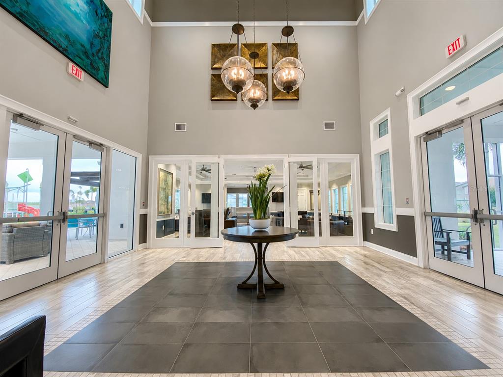 A bright, high-ceilinged lobby features a central round table, glass doors, and modern globe lighting — 3838 CAT MINT STREET, TAMPA, FL