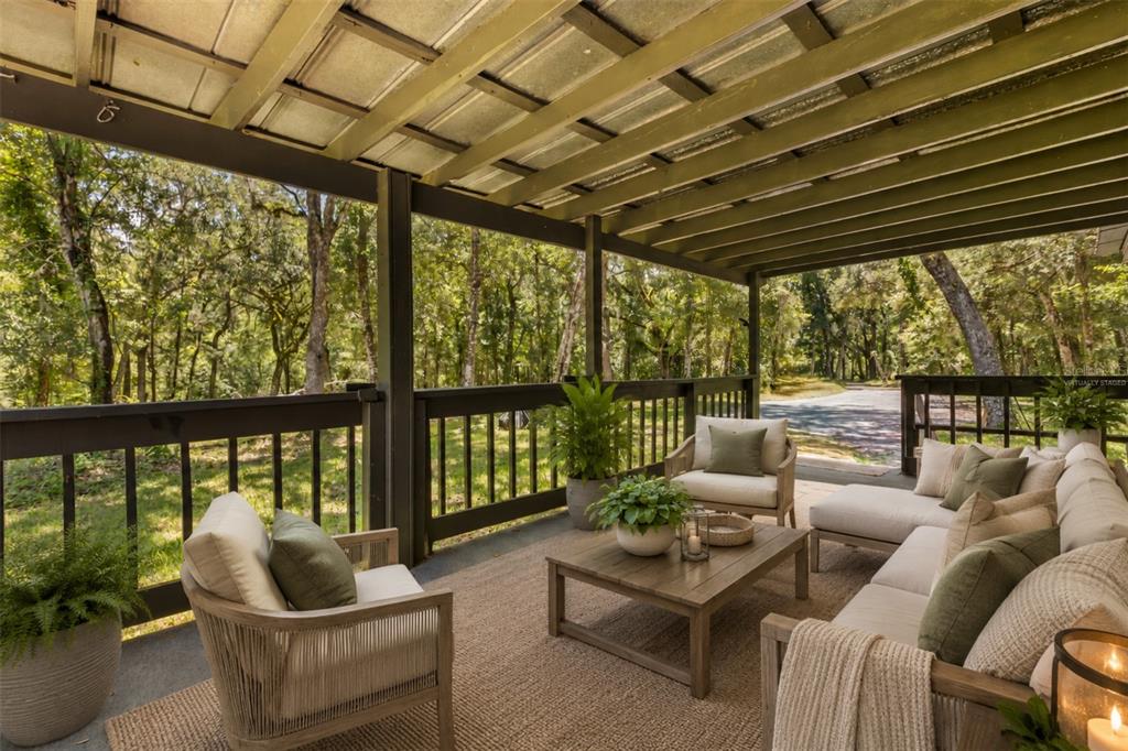 A covered outdoor patio features wooden furniture, a rug, and views of a wooded area — 3002 SW 127TH AVENUE, WEBSTER, FL