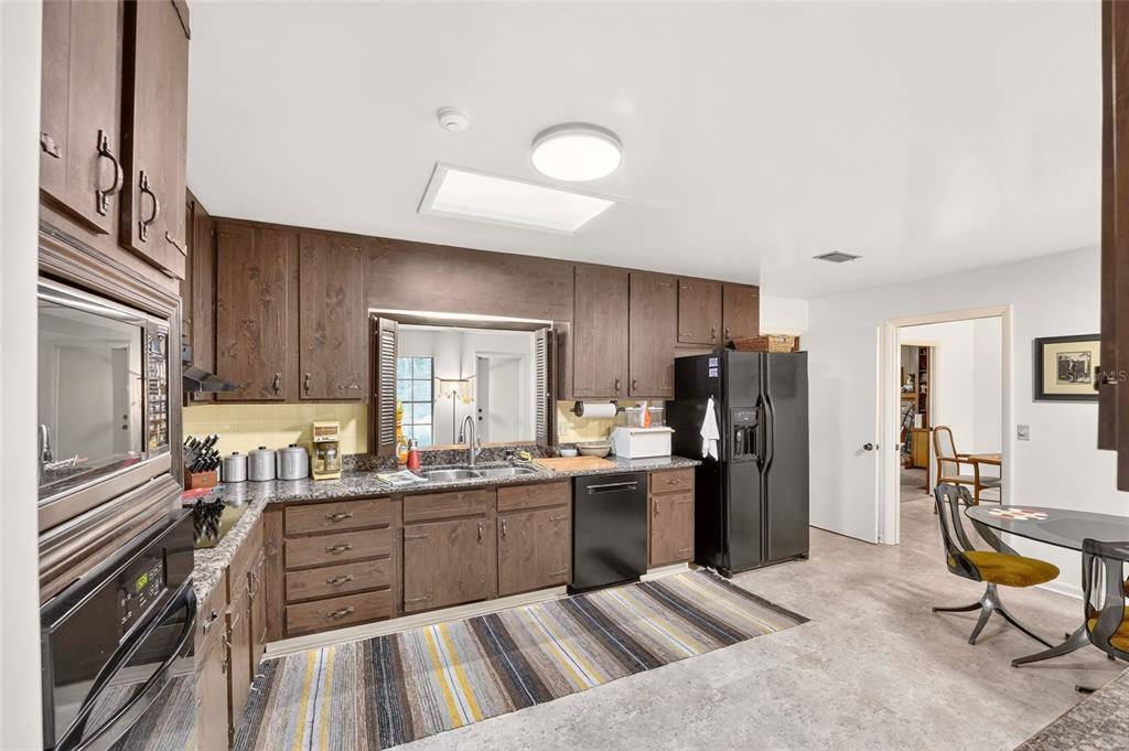 A kitchen with dark wood cabinets, granite countertops, black appliances, and a striped area rug — 4624 NW 19TH PLACE, GAINESVILLE, FL