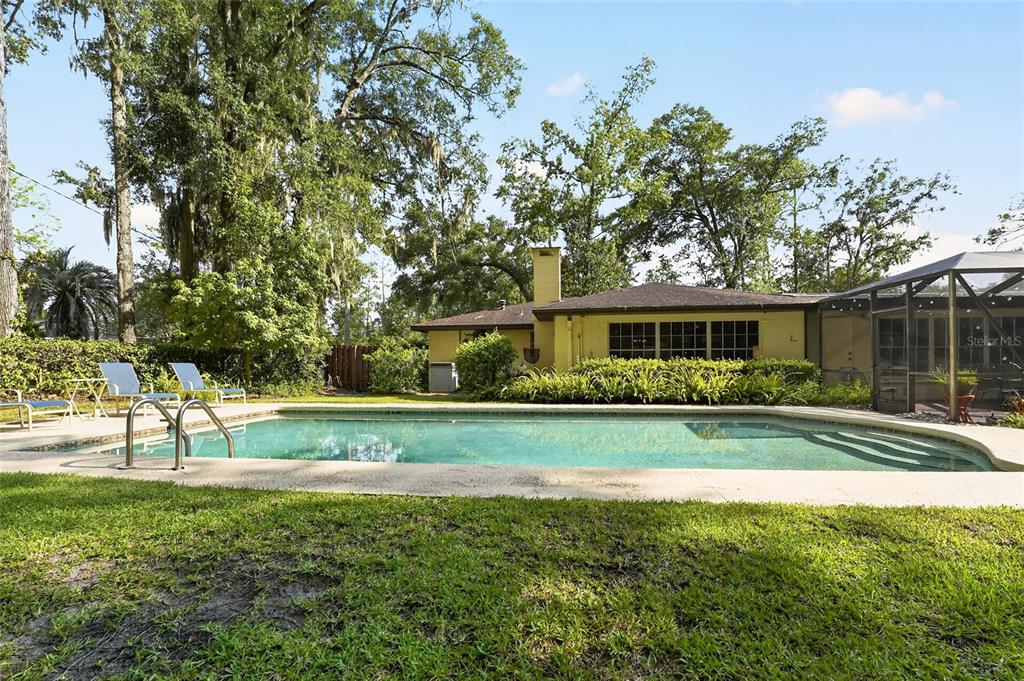 A backyard swimming pool sits in front of a single-story house with a screened patio — 4624 NW 19TH PLACE, GAINESVILLE, FL