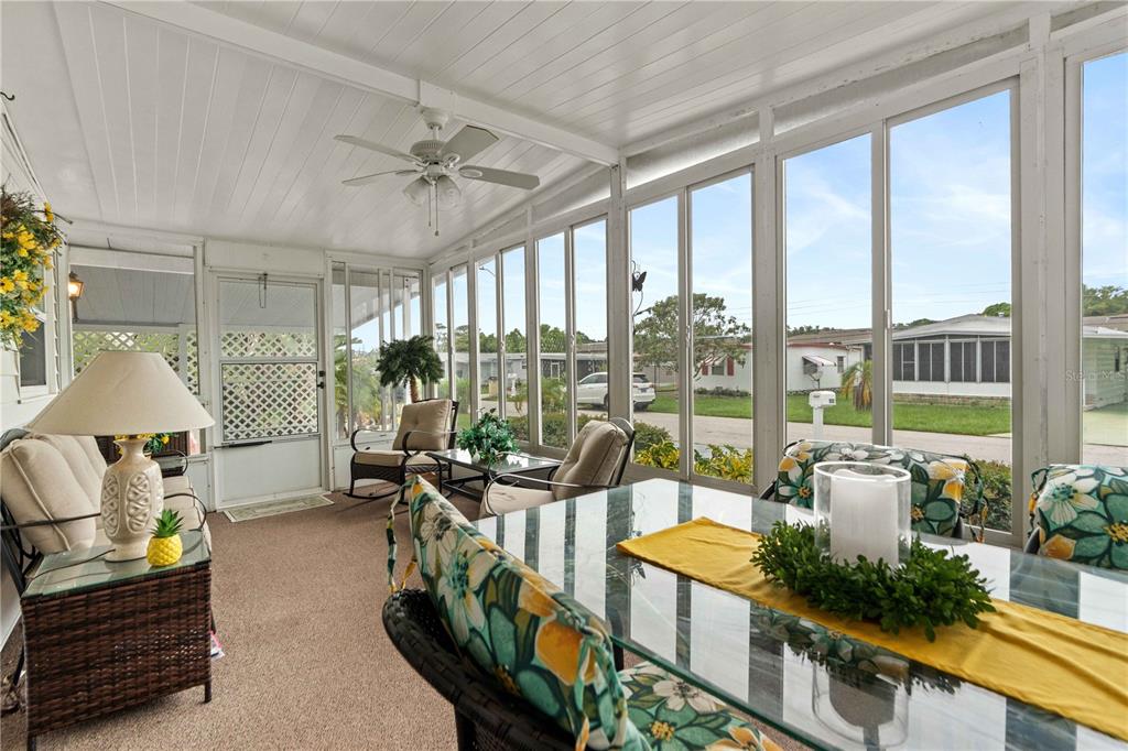 A sunroom features a glass dining table, wicker seating, a ceiling fan, and large windows — 5132 BOTANY DRIVE, HOLIDAY, FL