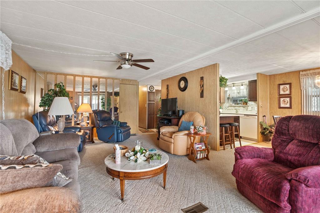 A living room features wood-paneled walls, carpeted flooring, a ceiling fan, and an open kitchen — 5132 BOTANY DRIVE, HOLIDAY, FL