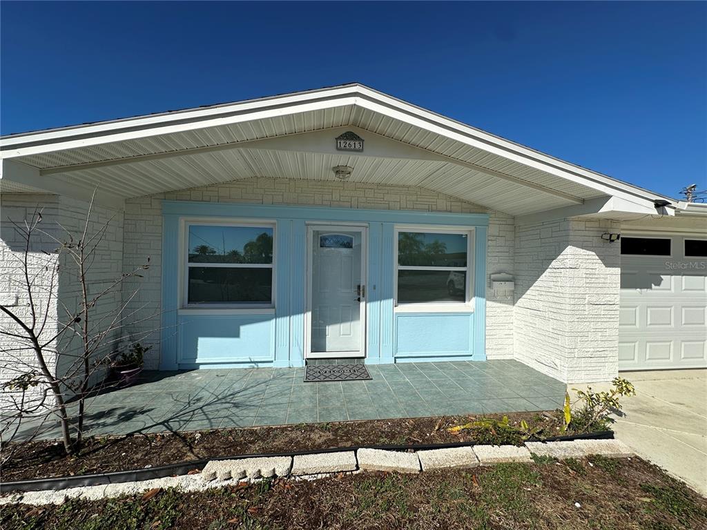 The exterior of a single-story house features white brick siding, a tiled porch, and light blue trim — 12613 4TH ISLE, HUDSON, FL