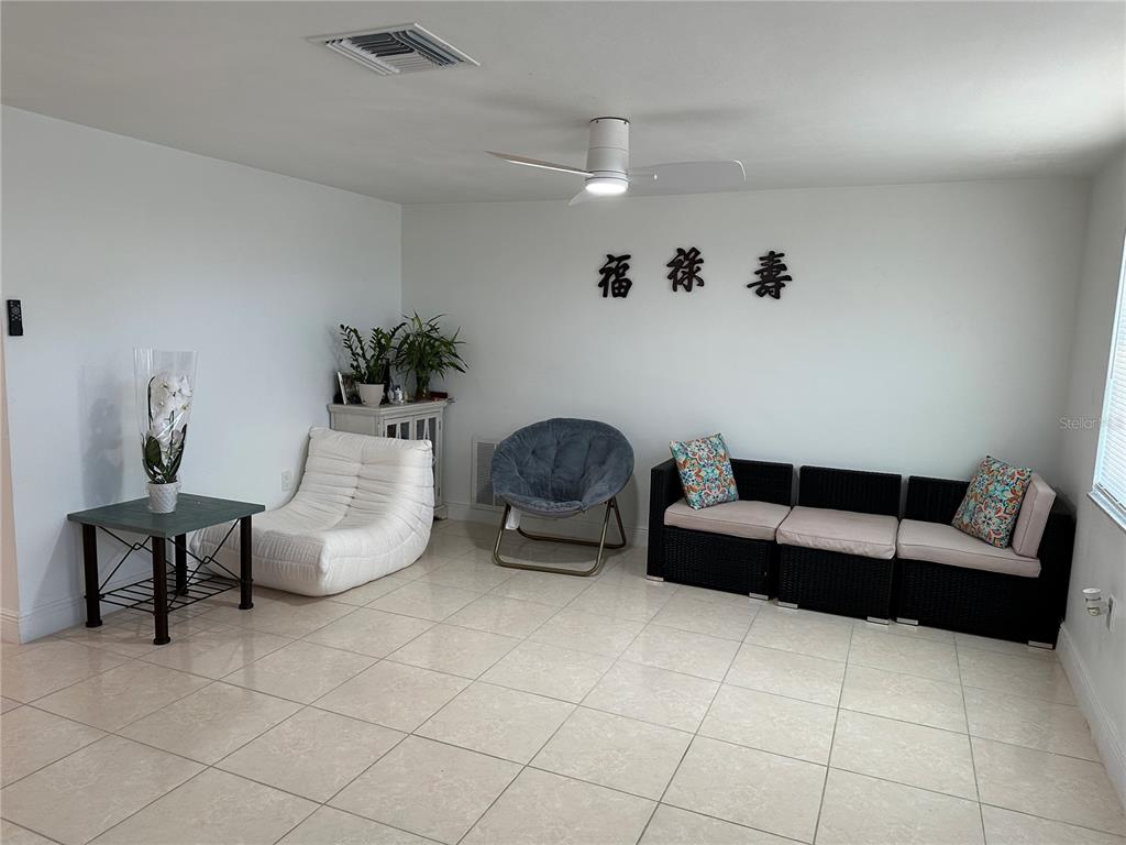 A living room features white walls, tile flooring, a ceiling fan, and various seating options — 12613 4TH ISLE, HUDSON, FL