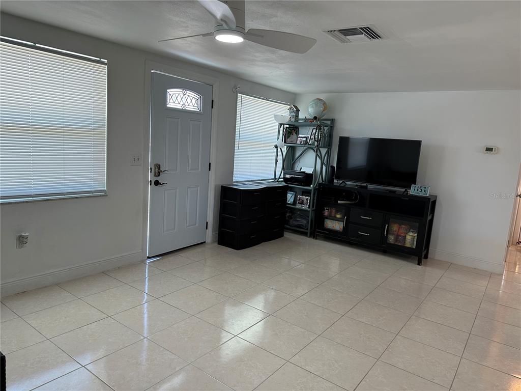 A living room features white walls, tile flooring, a ceiling fan, and a television console — 12613 4TH ISLE, HUDSON, FL
