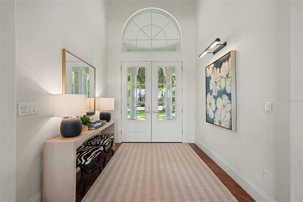 A bright foyer features a striped rug, a console table with lamps, and double glass doors — 3450 FOXMEADOW COURT, LONGWOOD, FL