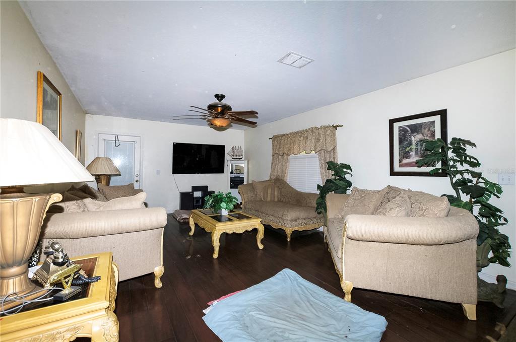 A living room features beige sofas, a wooden coffee table, dark flooring, and a ceiling fan — 5200 SW 115TH STREET ROAD, OCALA, FL