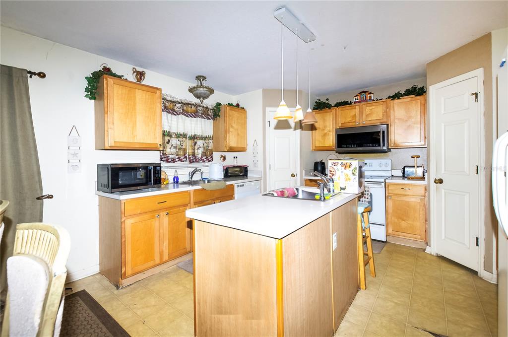A kitchen features light wood cabinets, a central island with a sink, and white appliances — 5200 SW 115TH STREET ROAD, OCALA, FL