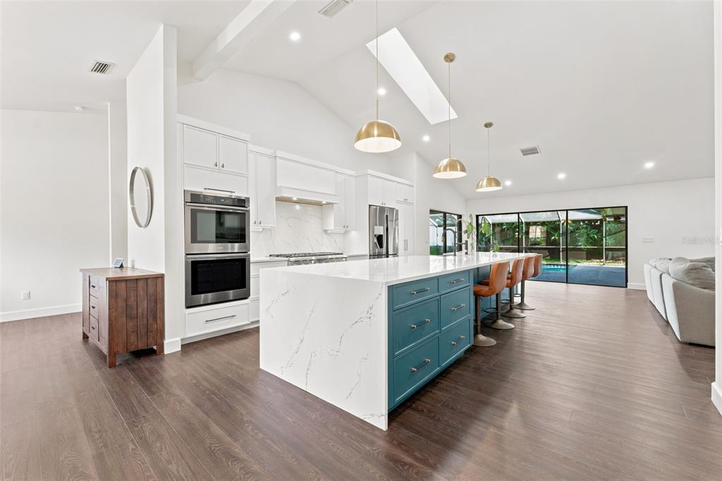 A modern kitchen features a large white marble island, teal cabinetry, and stainless steel appliances — 3969 TALAH DRIVE, PALM HARBOR, FL