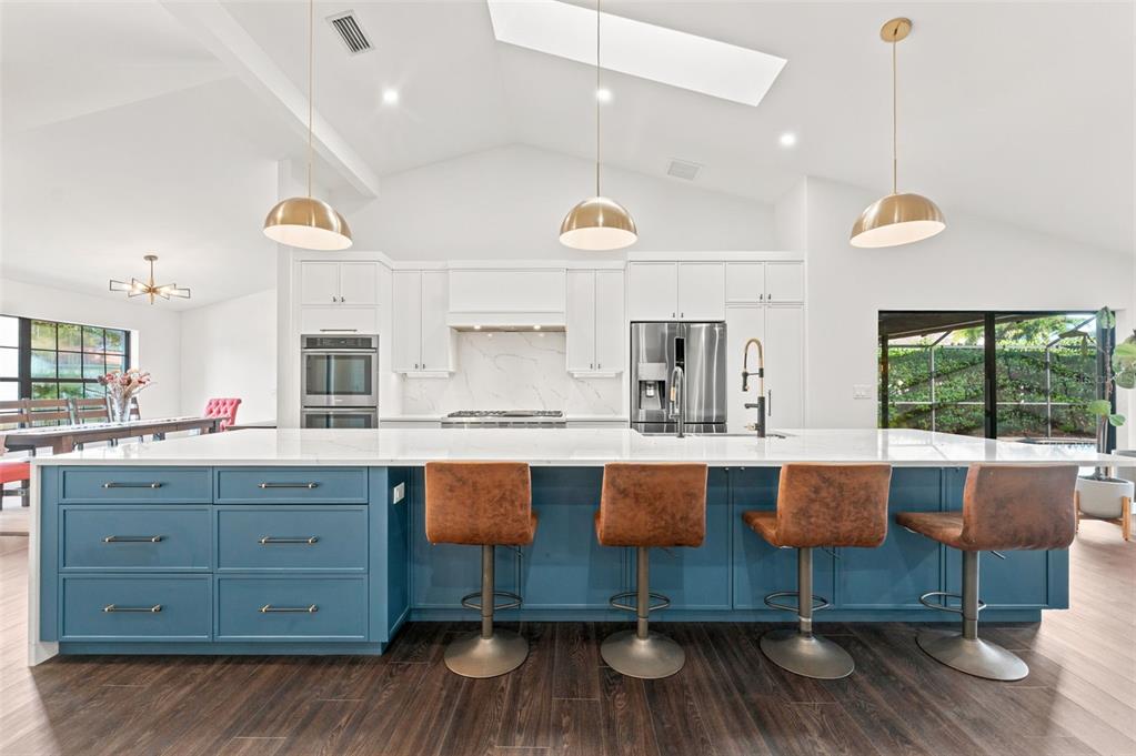 A modern kitchen features a large blue island with bar stools and white cabinetry — 3969 TALAH DRIVE, PALM HARBOR, FL