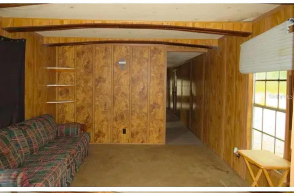 A living room features wood-paneled walls, a plaid sofa, and a doorway leading to a hallway — 10130 208TH PATH, O'BRIEN, FL
