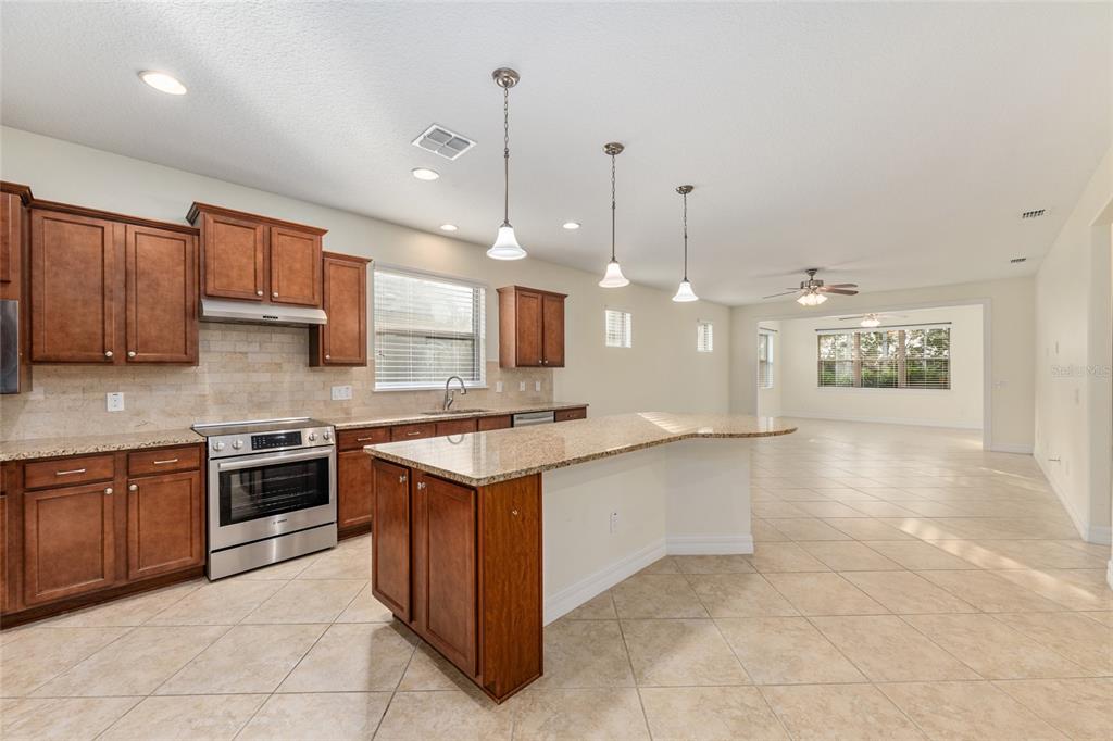 A kitchen with wood cabinets, granite countertops, and an island opens into a living area — 9221 SW 70TH LOOP, OCALA, FL